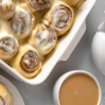 Freshly baked sourdough cinnamon rolls topped with cream cheese frosting on a rustic wooden table.