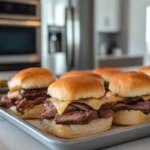 Tray of freshly baked roast beef sliders with melted cheese and golden buns on a modern kitchen countertop, ready to serve for parties or casual meals.